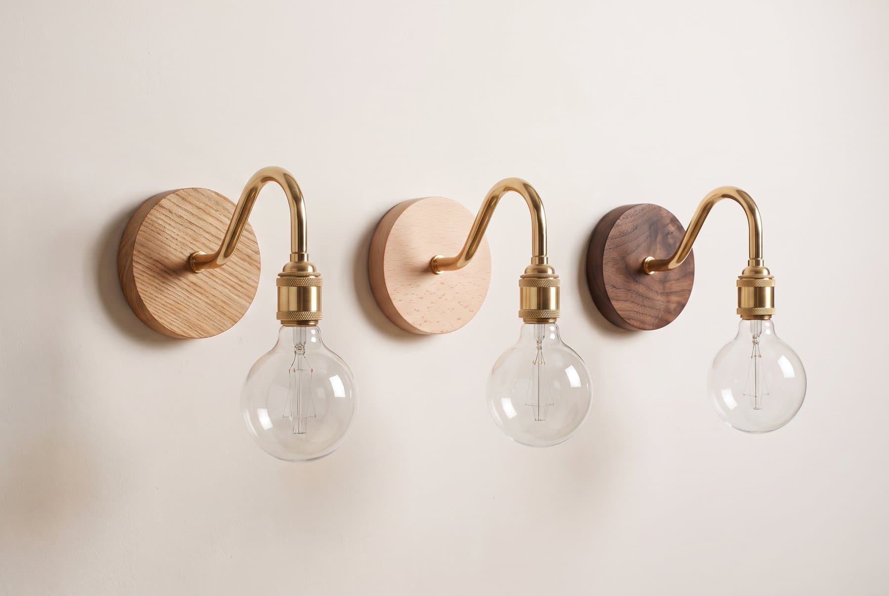 Three brass swan neck wall lights on oak, beech and walnut back plates in a row