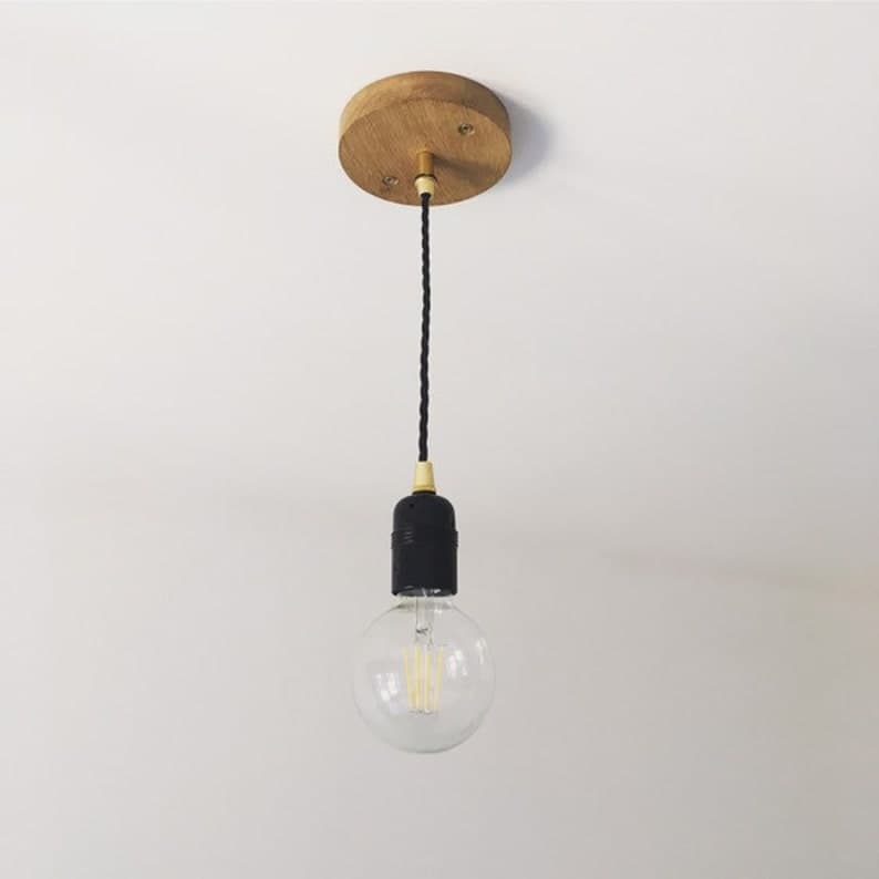 Pendant light hanging from a turned oak ceiling rose on black twisted fabric flex, with a brass holder and a globe bulb