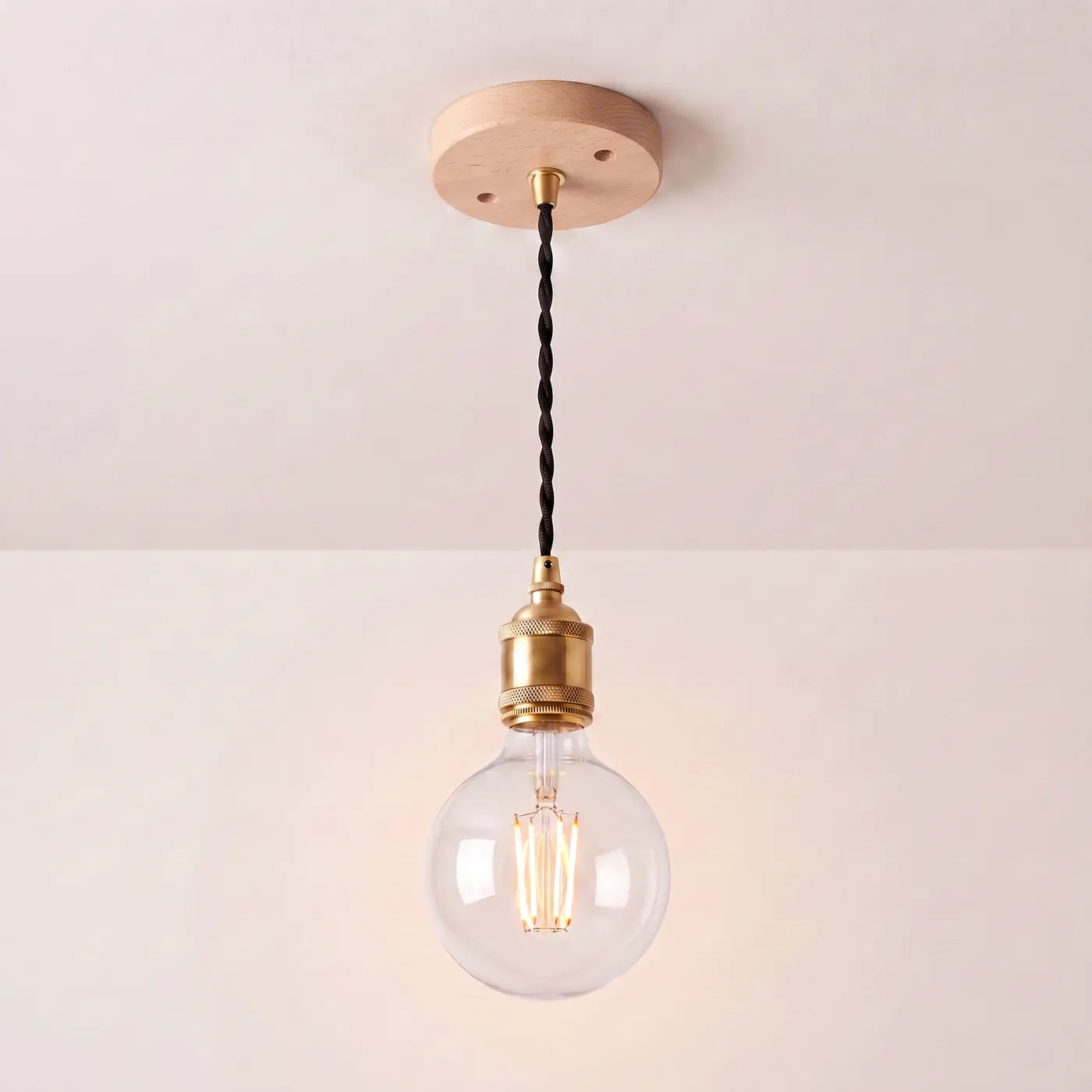 Pendant light with a turned beech ceiling rose, black twisted fabric flex and a brass bulb holder, lit with a clear globe filament bulb