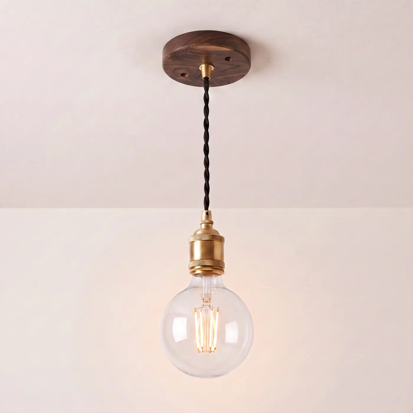 Pendant light with a turned walnut ceiling rose, black twisted fabric flex and a brass bulb holder, lit with a clear globe filament bulb