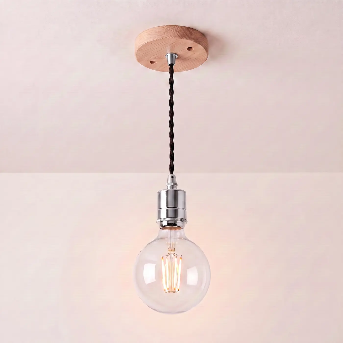 Pendant light with a turned natural oak ceiling rose, black twisted fabric flex and a chrome bulb holder, lit with a clear globe filament bulb