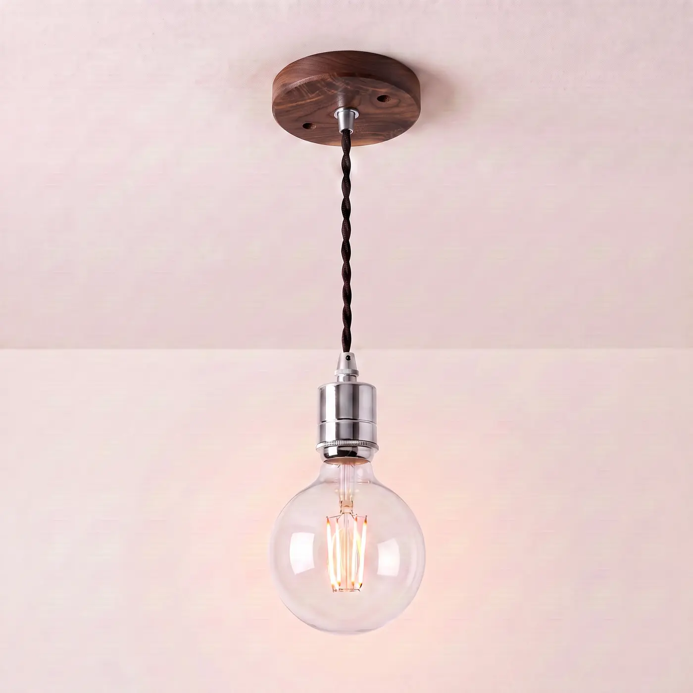 Pendant light with a turned walnut ceiling rose, black twisted fabric flex and a chrome bulb holder, lit with a clear globe filament bulb