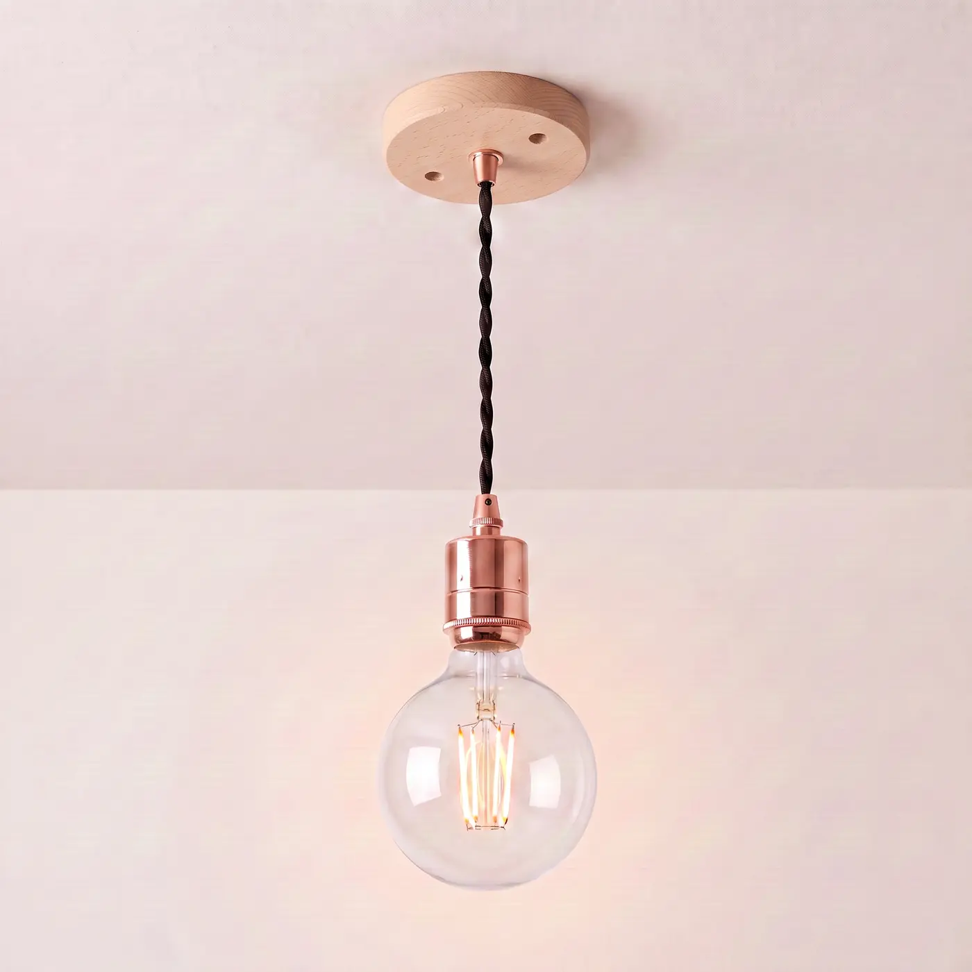 Pendant light with a turned beech ceiling rose, black twisted fabric flex and a copper bulb holder, lit with a clear globe filament bulb