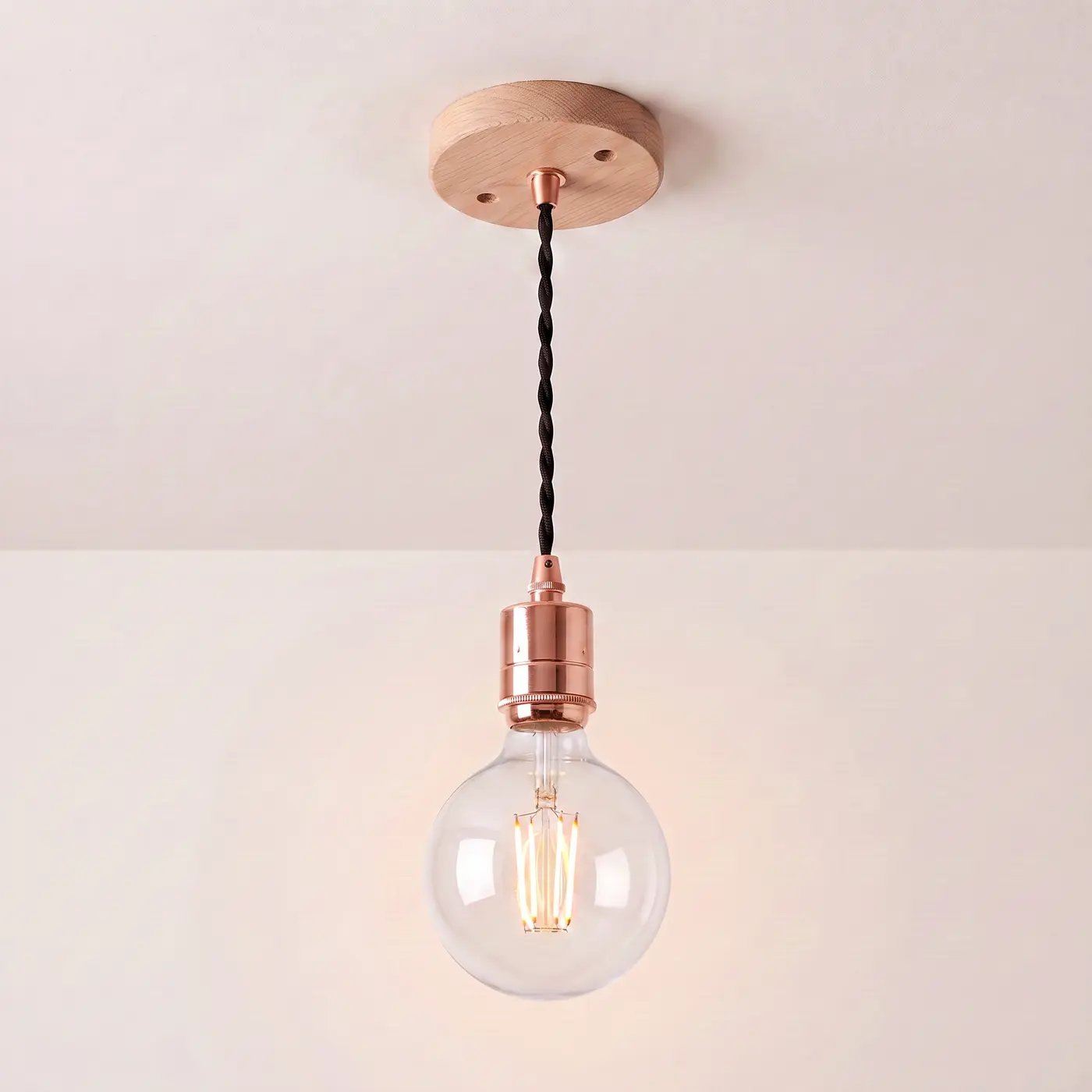 Pendant light with a turned natural oak ceiling rose, black twisted fabric flex and a copper bulb holder, lit with a clear globe filament bulb