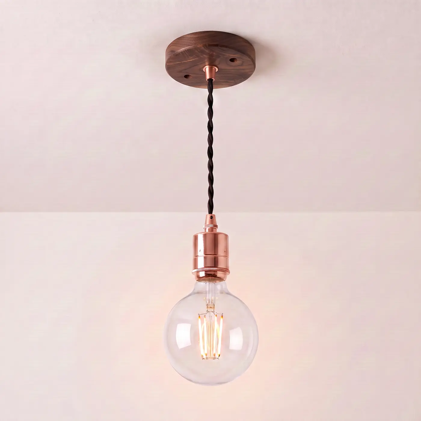 Pendant light with a turned walnut ceiling rose, black twisted fabric flex and a copper bulb holder, lit with a clear globe filament bulb