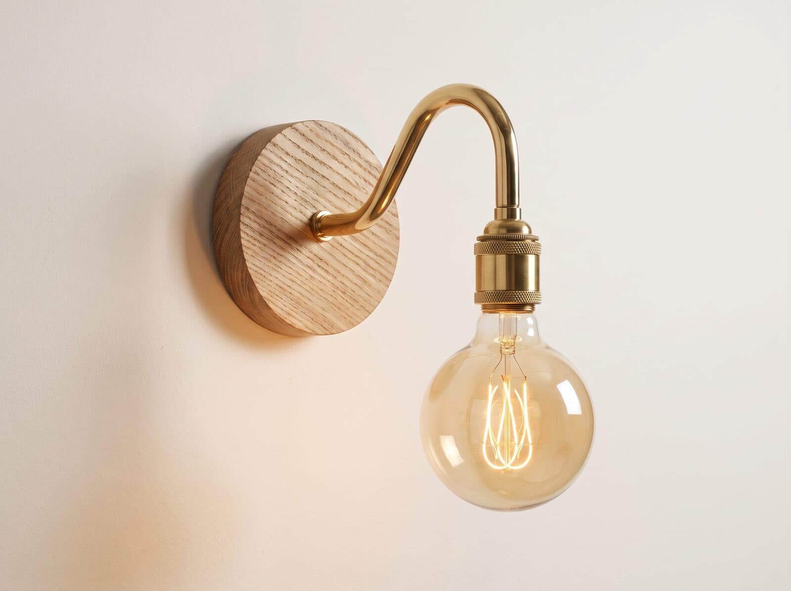 Brass swan neck wall light with an exposed globe bulb on a turned oak plate