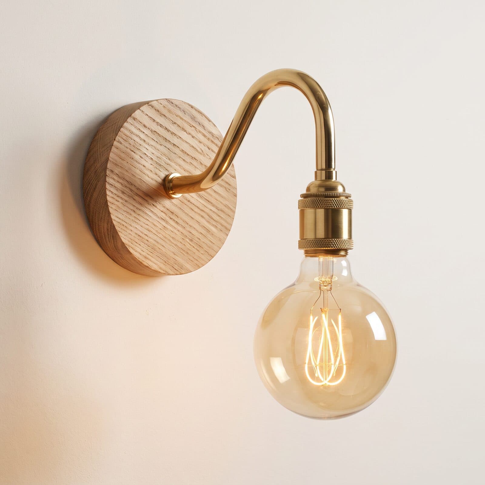 Swan neck wall light with a clear globe filament bulb in a brass holder, on an oak back plate