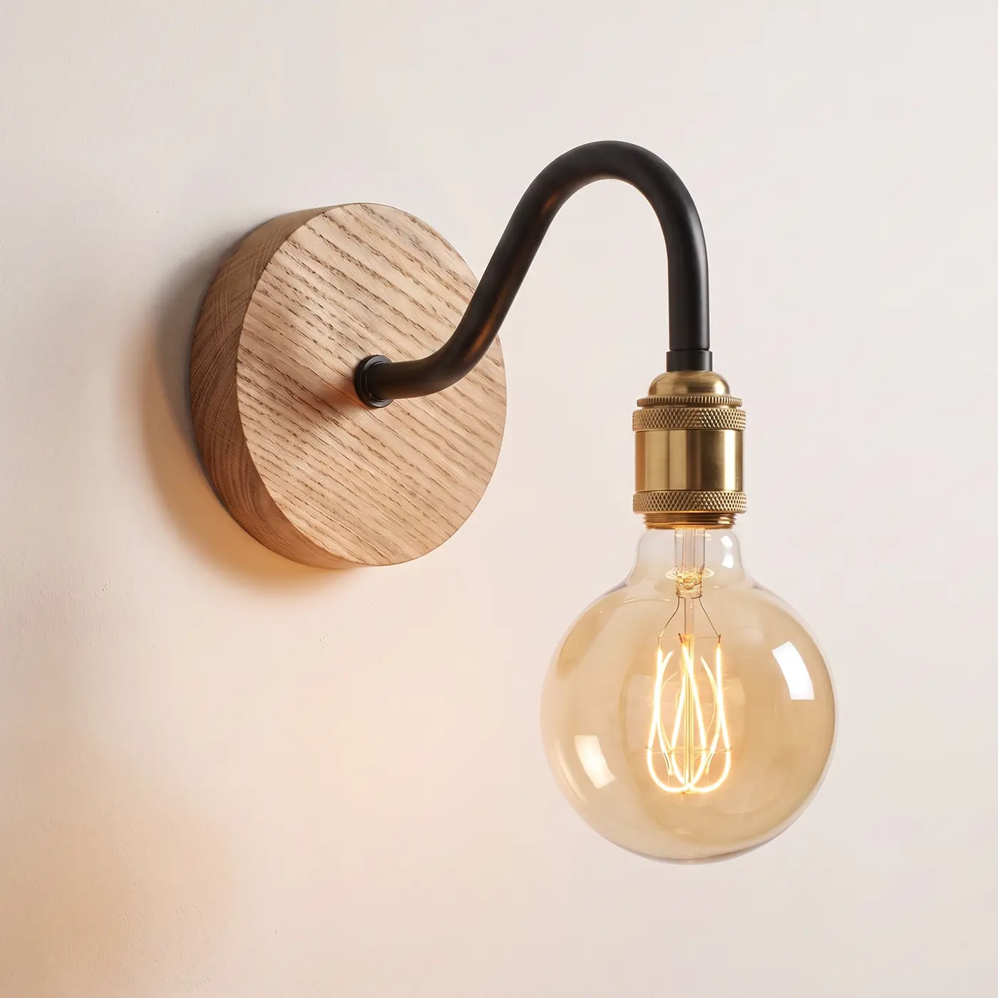 Swan neck wall light with a natural oak back plate, black swan neck arm and brass bulb holder, lit with a globe filament bulb