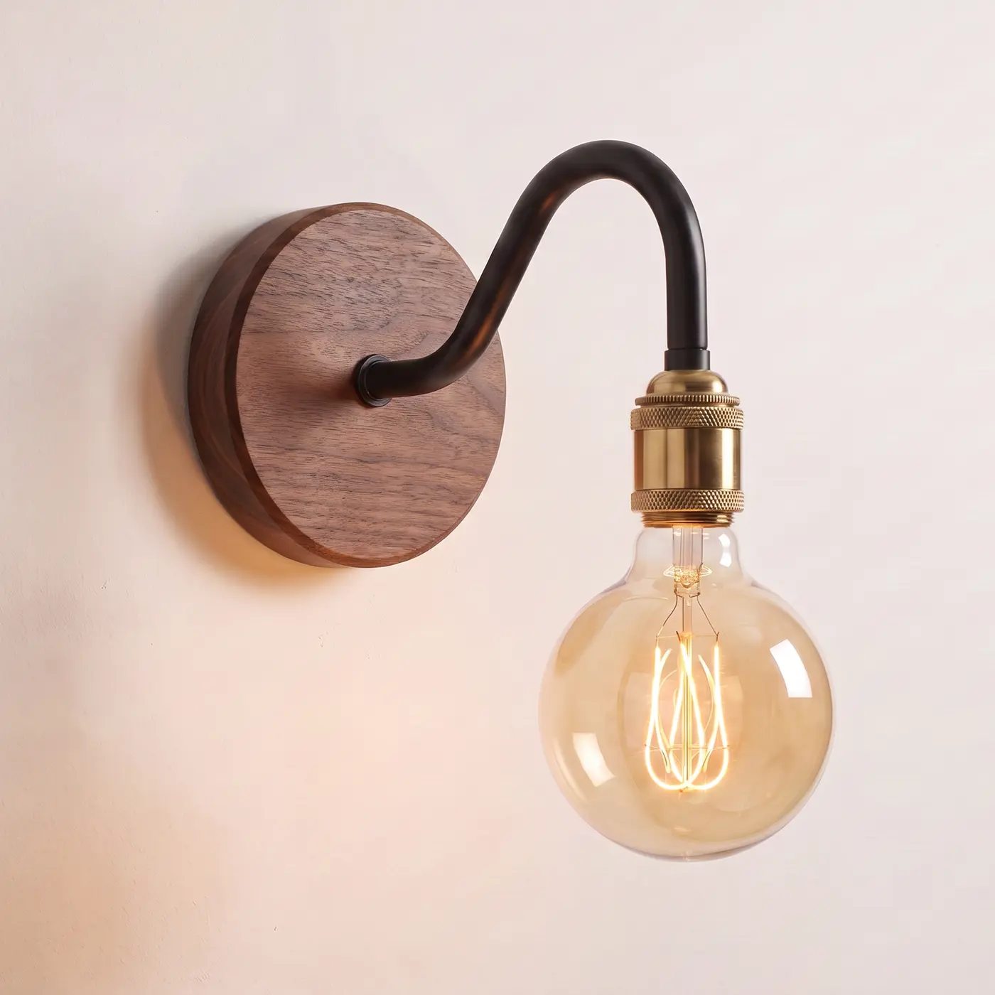 Swan neck wall light with a walnut back plate, black swan neck arm and brass bulb holder, lit with a globe filament bulb