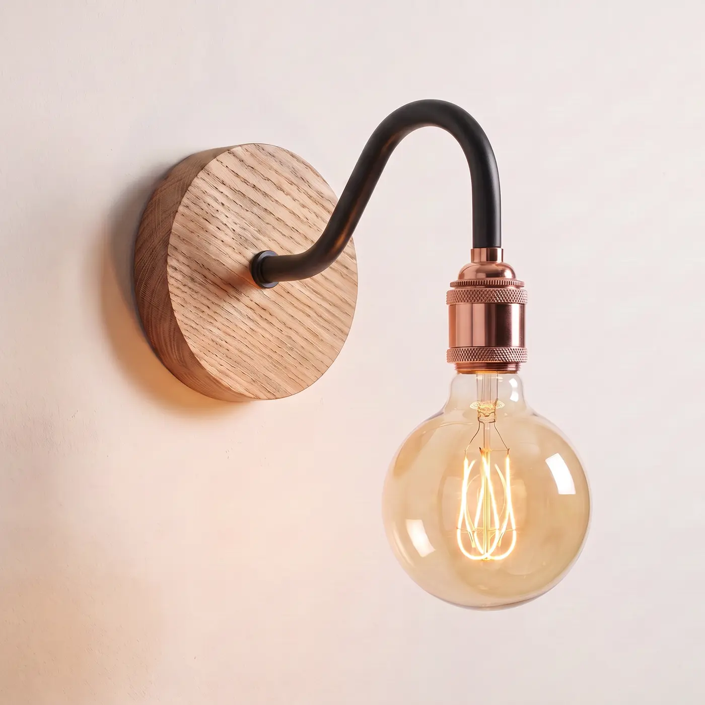 Swan neck wall light with a natural oak back plate, black swan neck arm and copper bulb holder, lit with a globe filament bulb