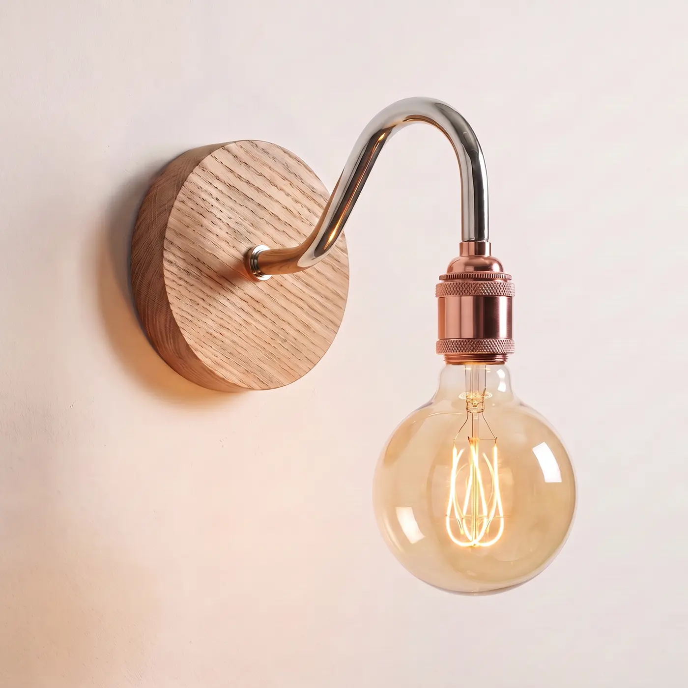 Swan neck wall light with a natural oak back plate, chrome swan neck arm and copper bulb holder, lit with a globe filament bulb