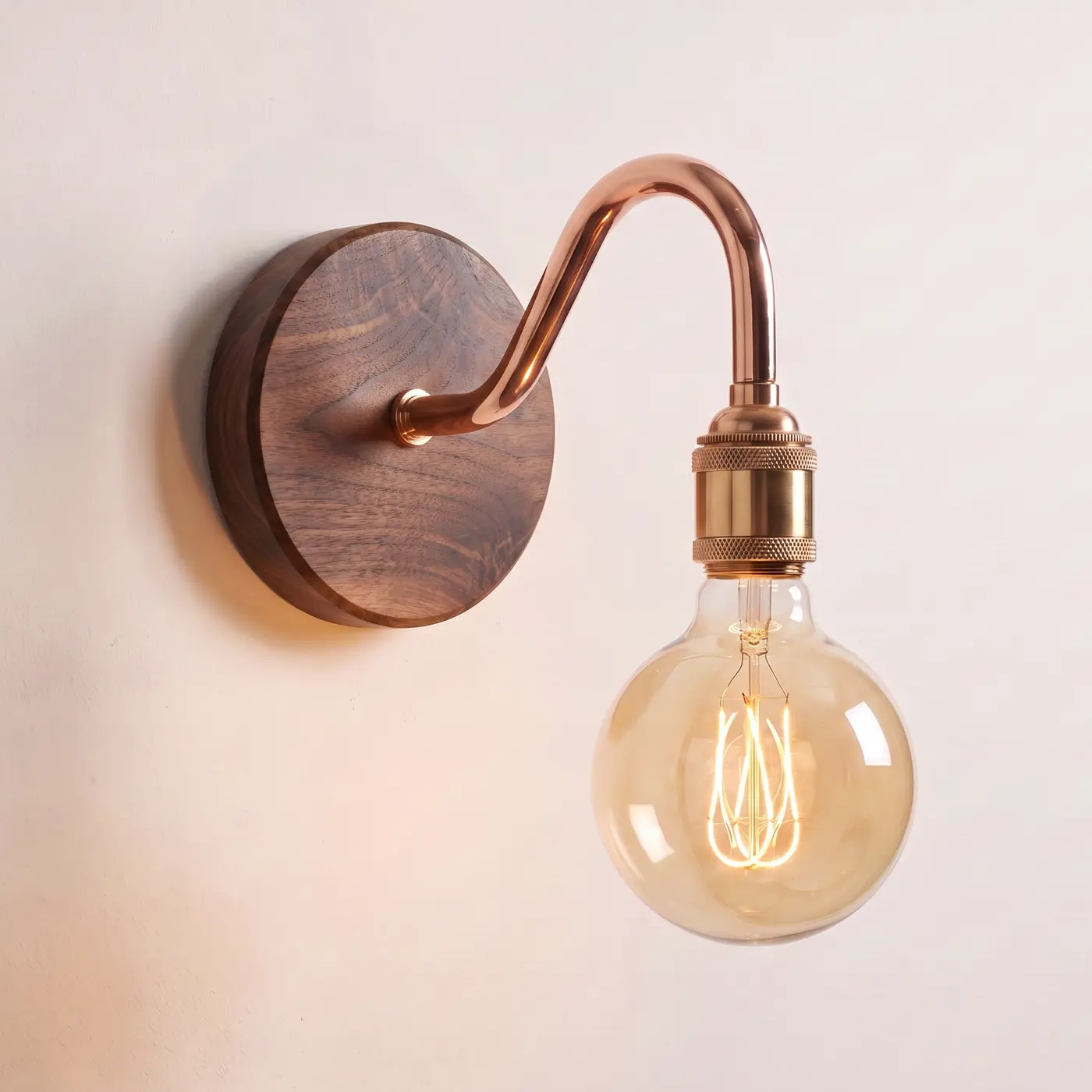 Swan neck wall light with a walnut back plate, copper swan neck arm and brass bulb holder, lit with a globe filament bulb
