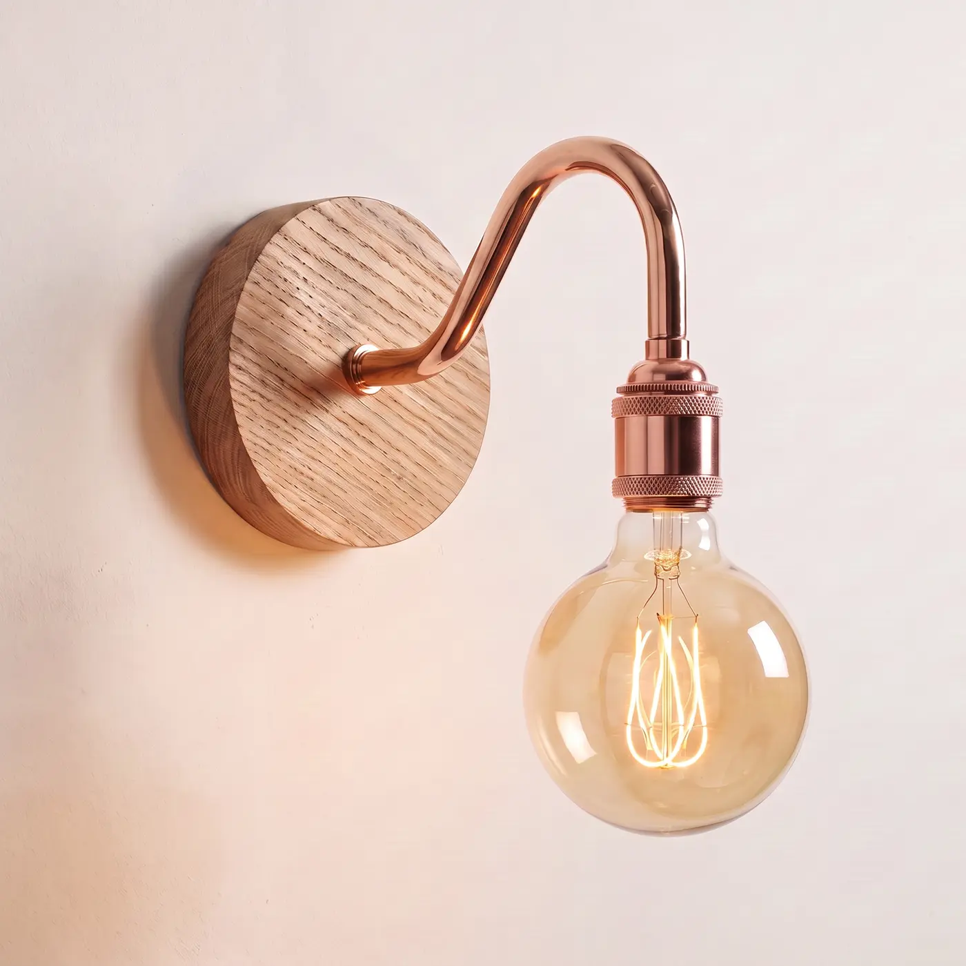 Swan neck wall light with a natural oak back plate, copper swan neck arm and matching bulb holder, lit with a globe filament bulb
