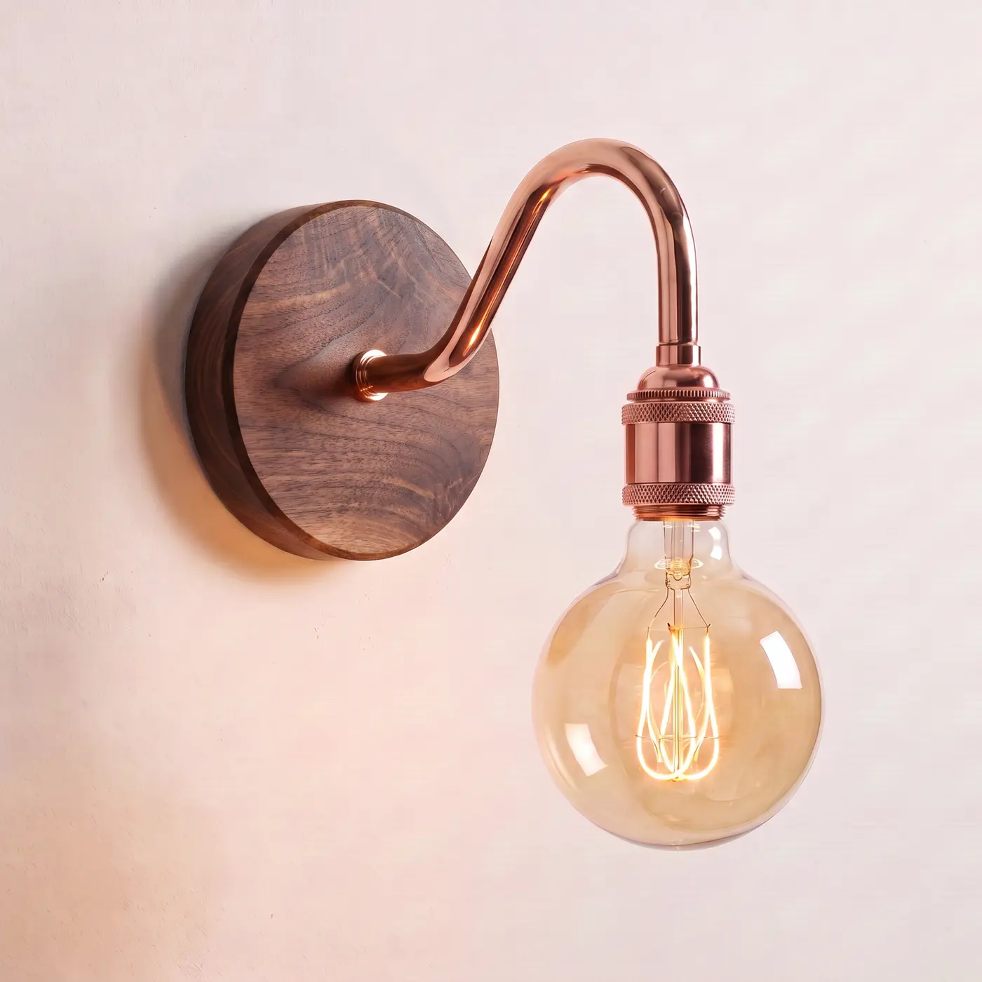Swan neck wall light with a walnut back plate, copper swan neck arm and matching bulb holder, lit with a globe filament bulb