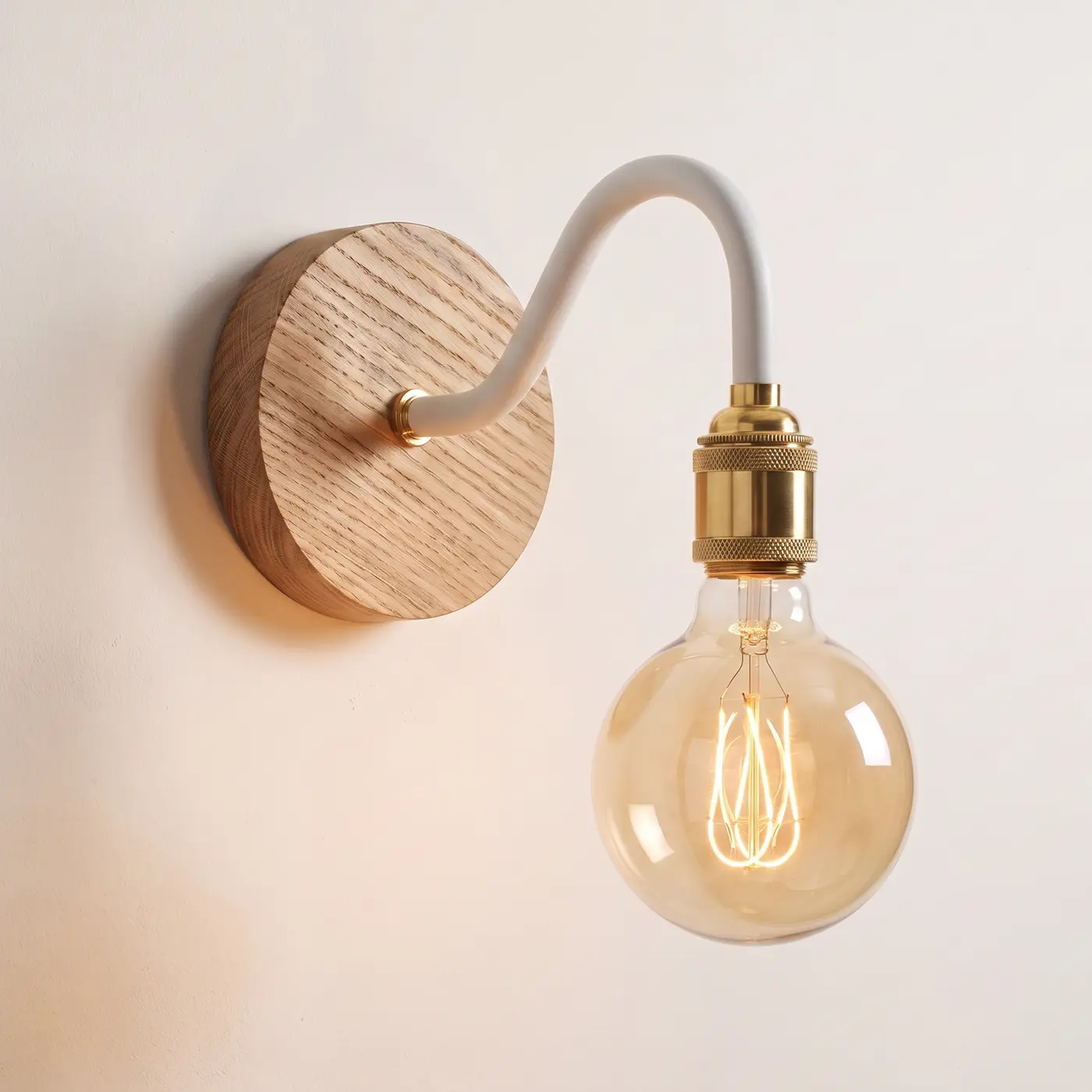 Swan neck wall light with a natural oak back plate, white swan neck arm and brass bulb holder, lit with a globe filament bulb