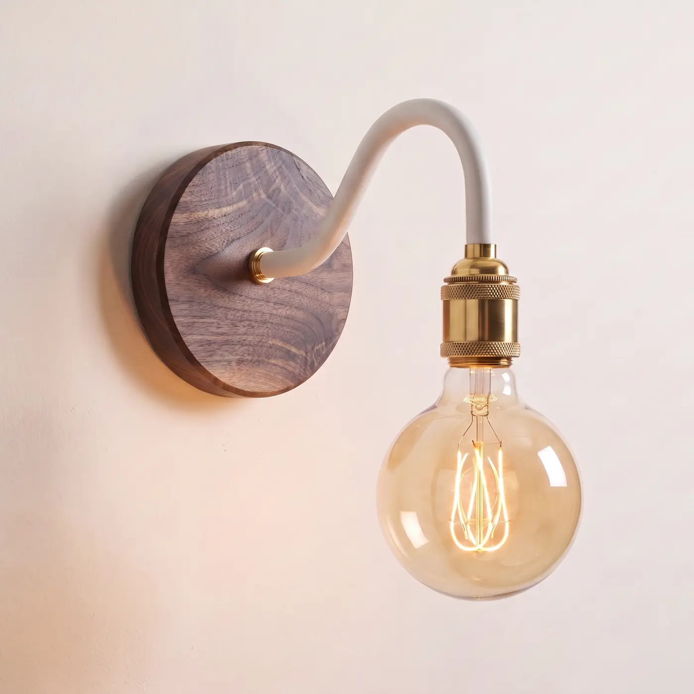Swan neck wall light with a walnut back plate, white swan neck arm and brass bulb holder, lit with a globe filament bulb
