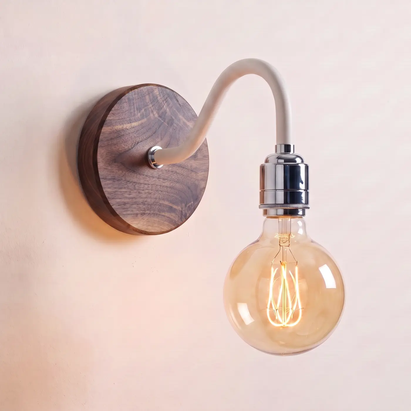 Swan neck wall light with a walnut back plate, white swan neck arm and chrome bulb holder, lit with a globe filament bulb