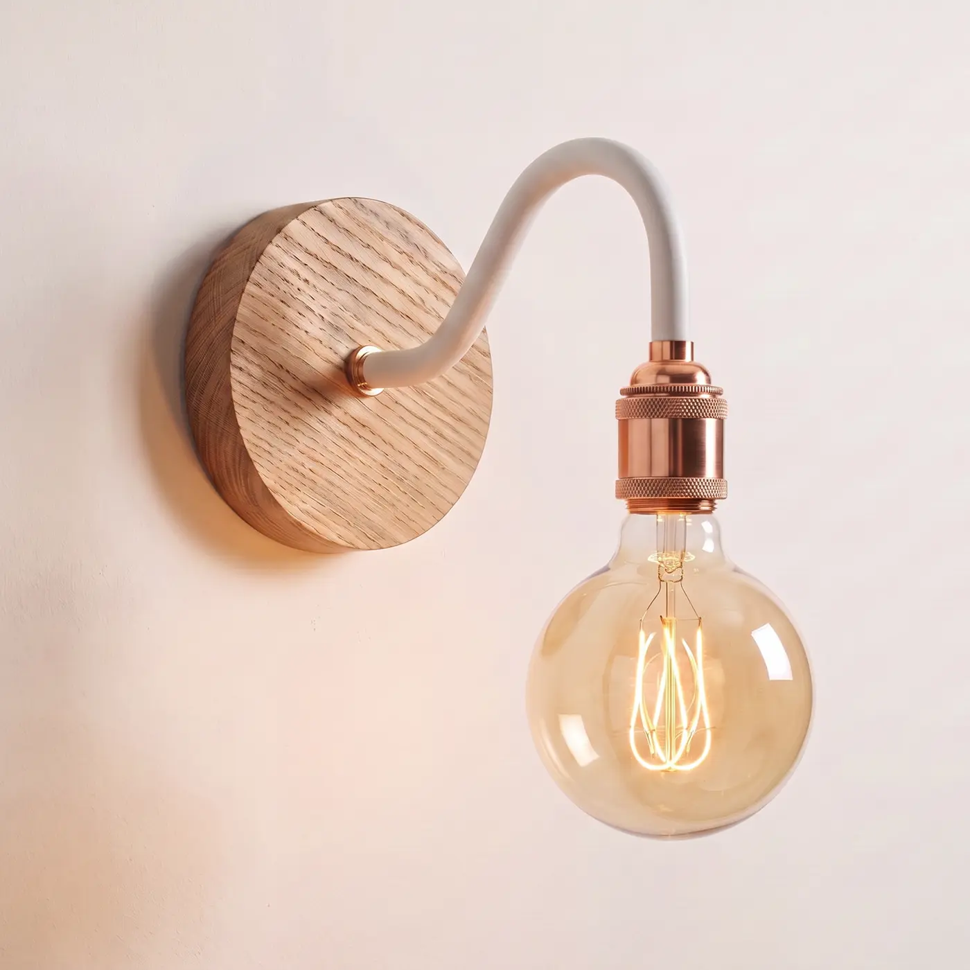 Swan neck wall light with a natural oak back plate, white swan neck arm and copper bulb holder, lit with a globe filament bulb
