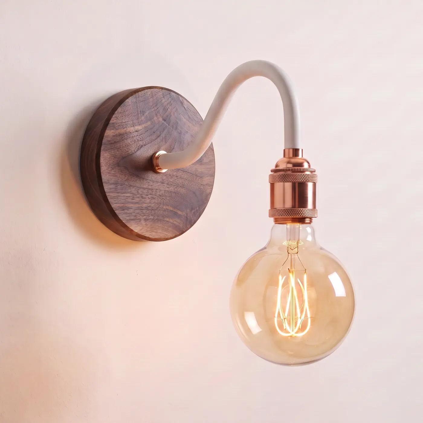 Swan neck wall light with a walnut back plate, white swan neck arm and copper bulb holder, lit with a globe filament bulb